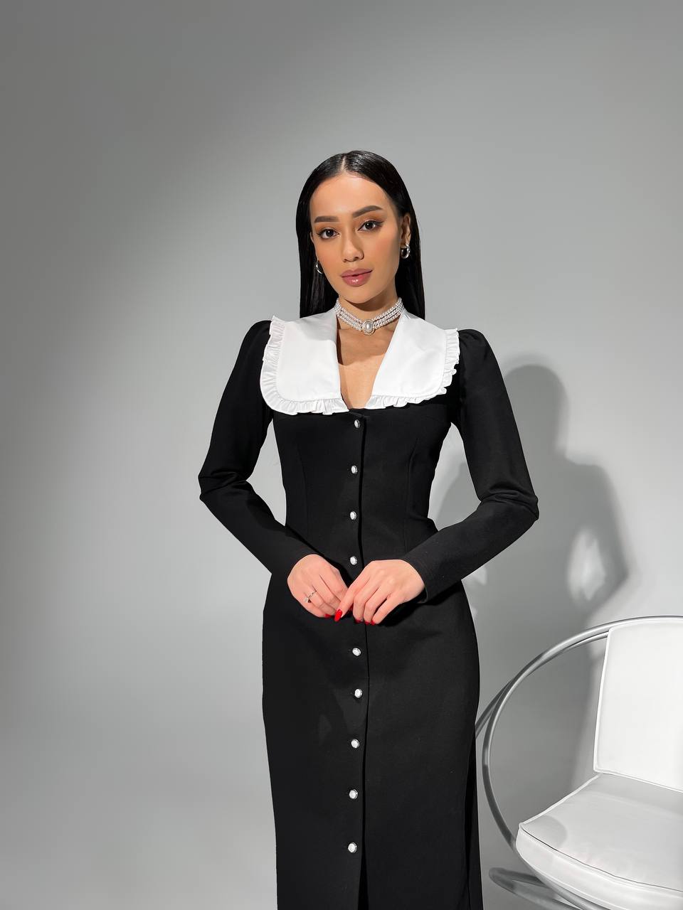 Woman wearing a black dress with white collar against a gray background