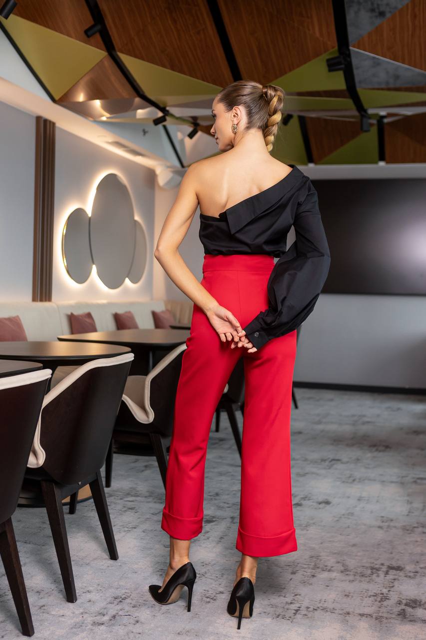 Woman in a black top and red pants standing in a modern restaurant.