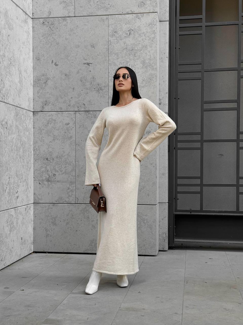 Woman in a long, light-colored dress standing against a concrete wall.