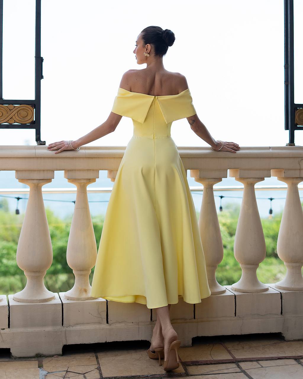 Woman in a yellow off-shoulder dress standing on a balcony.