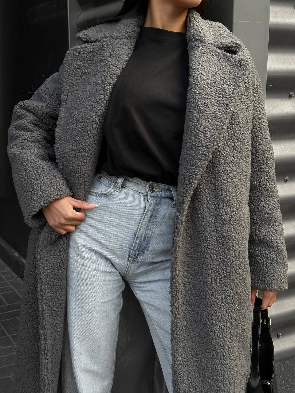 Person wearing a long gray coat, black top, and light blue jeans.