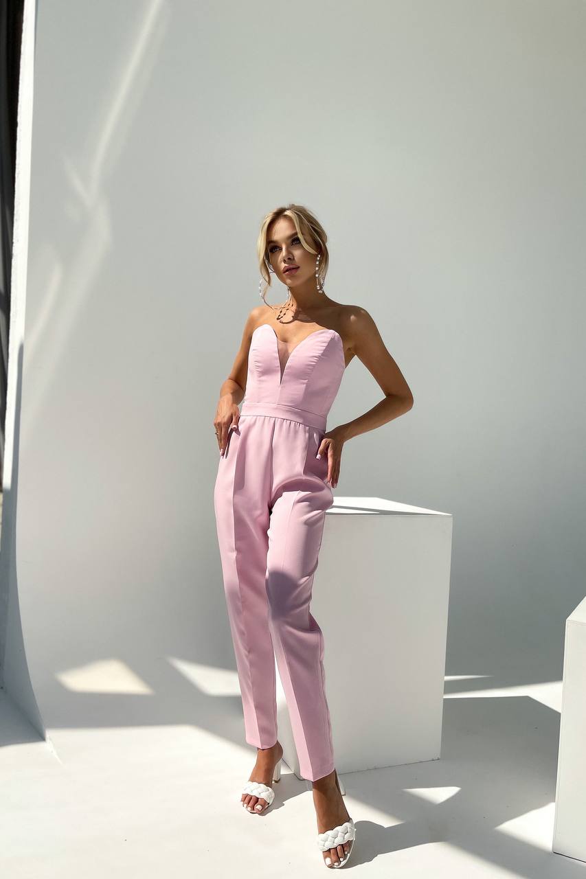 Woman wearing a pink strapless jumpsuit standing against a white background