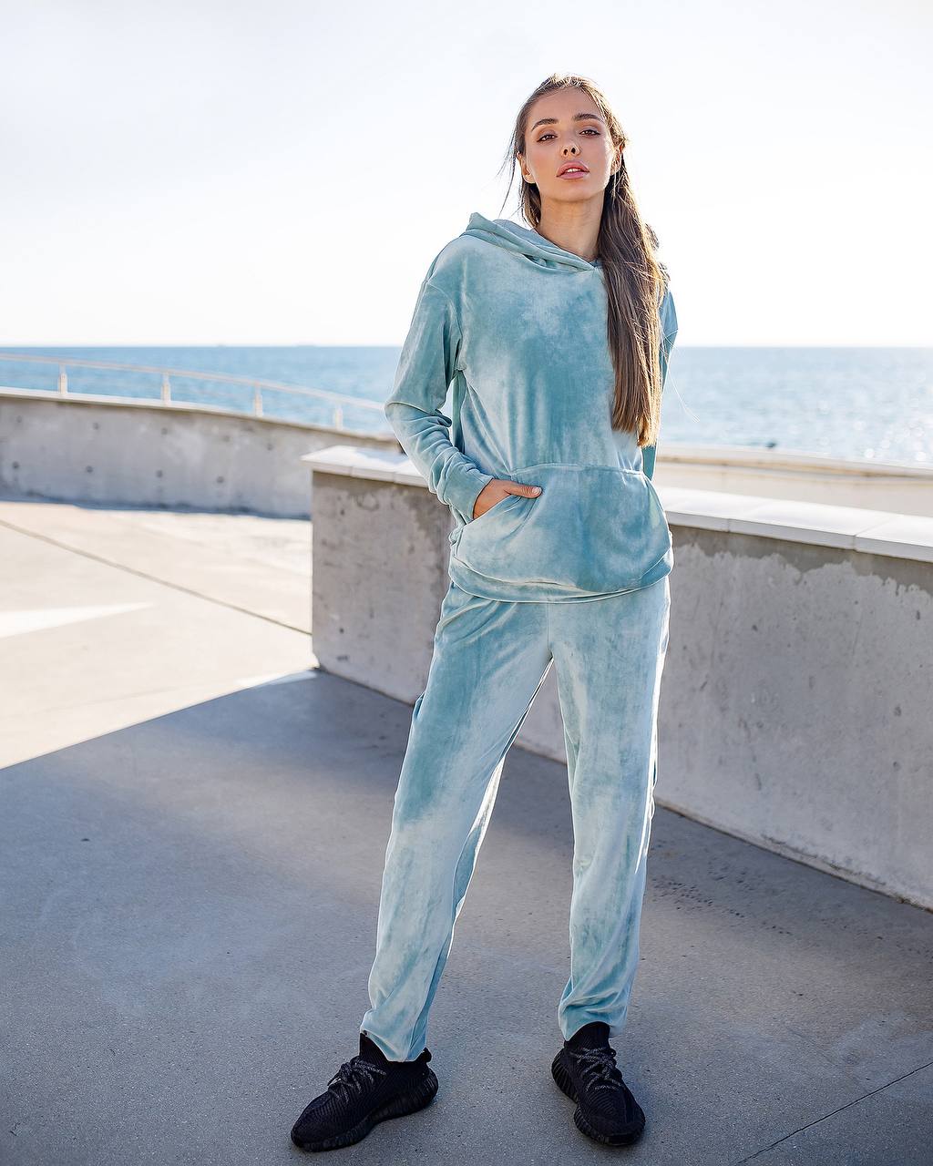 Woman in a light blue tracksuit standing on a rooftop with ocean view