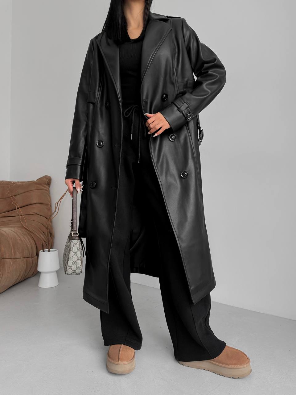 Person wearing a long black leather coat in a minimal indoor setting