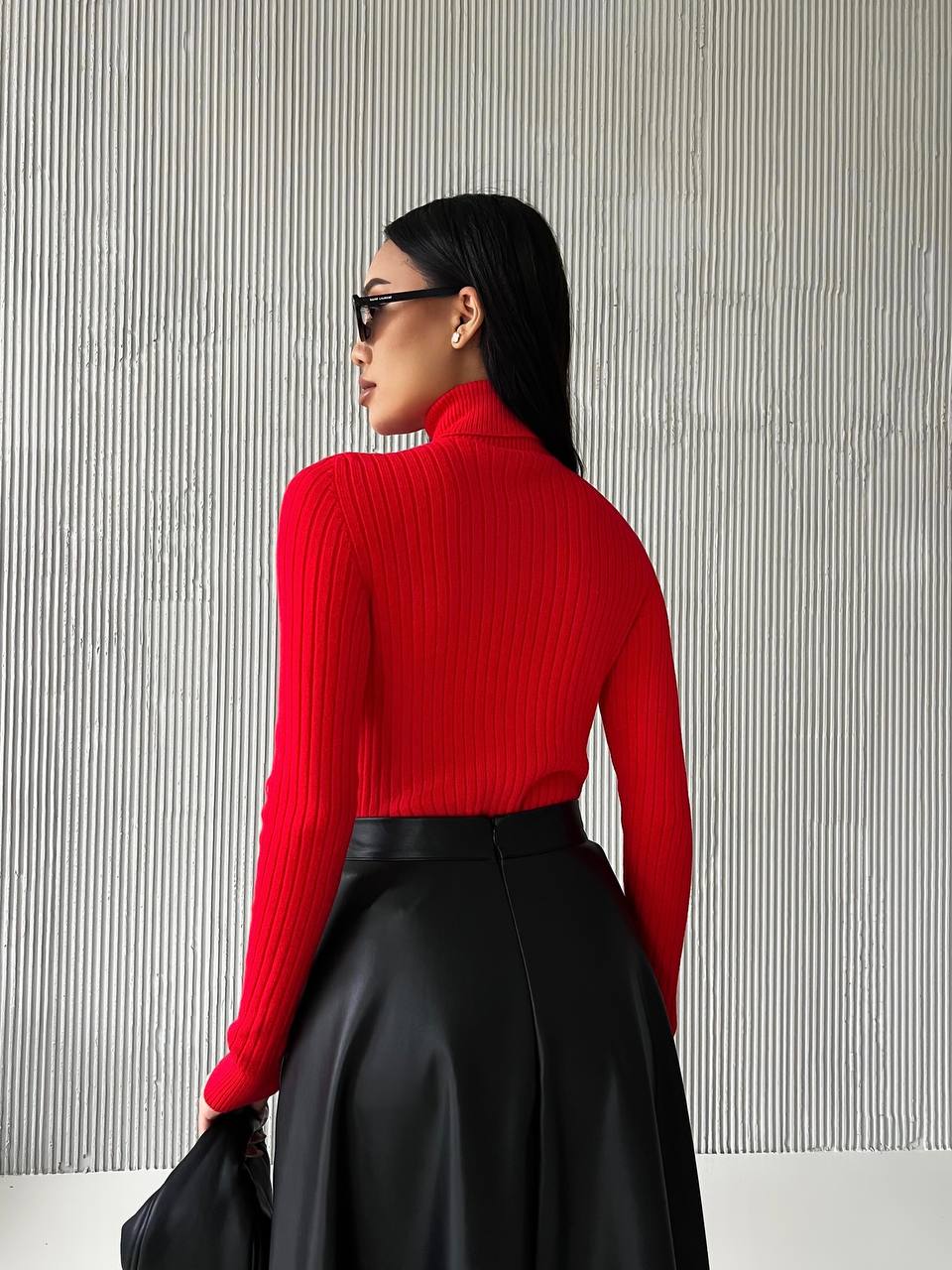 Woman wearing a red sweater and black skirt against a gray striped wall