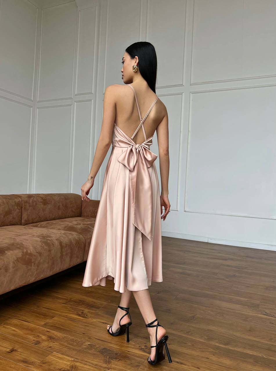 Woman in a pink dress standing in a room with wooden flooring and a brown sofa.