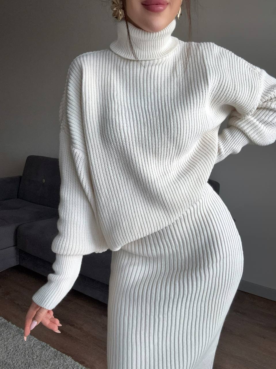 Person wearing a white ribbed knit outfit in a room with a gray couch.