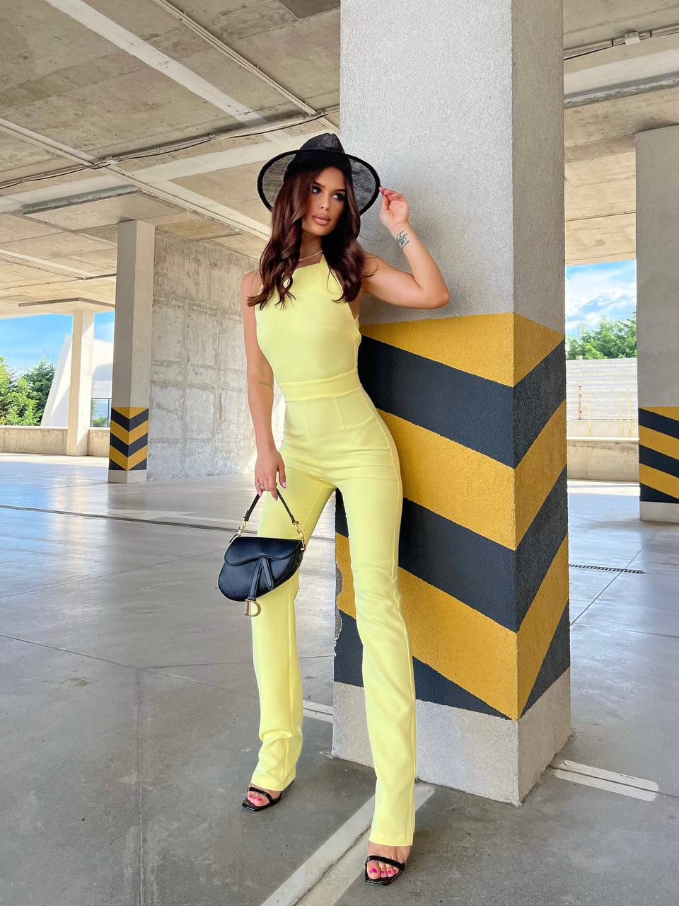 Woman in a yellow jumpsuit posing against a geometric wall.