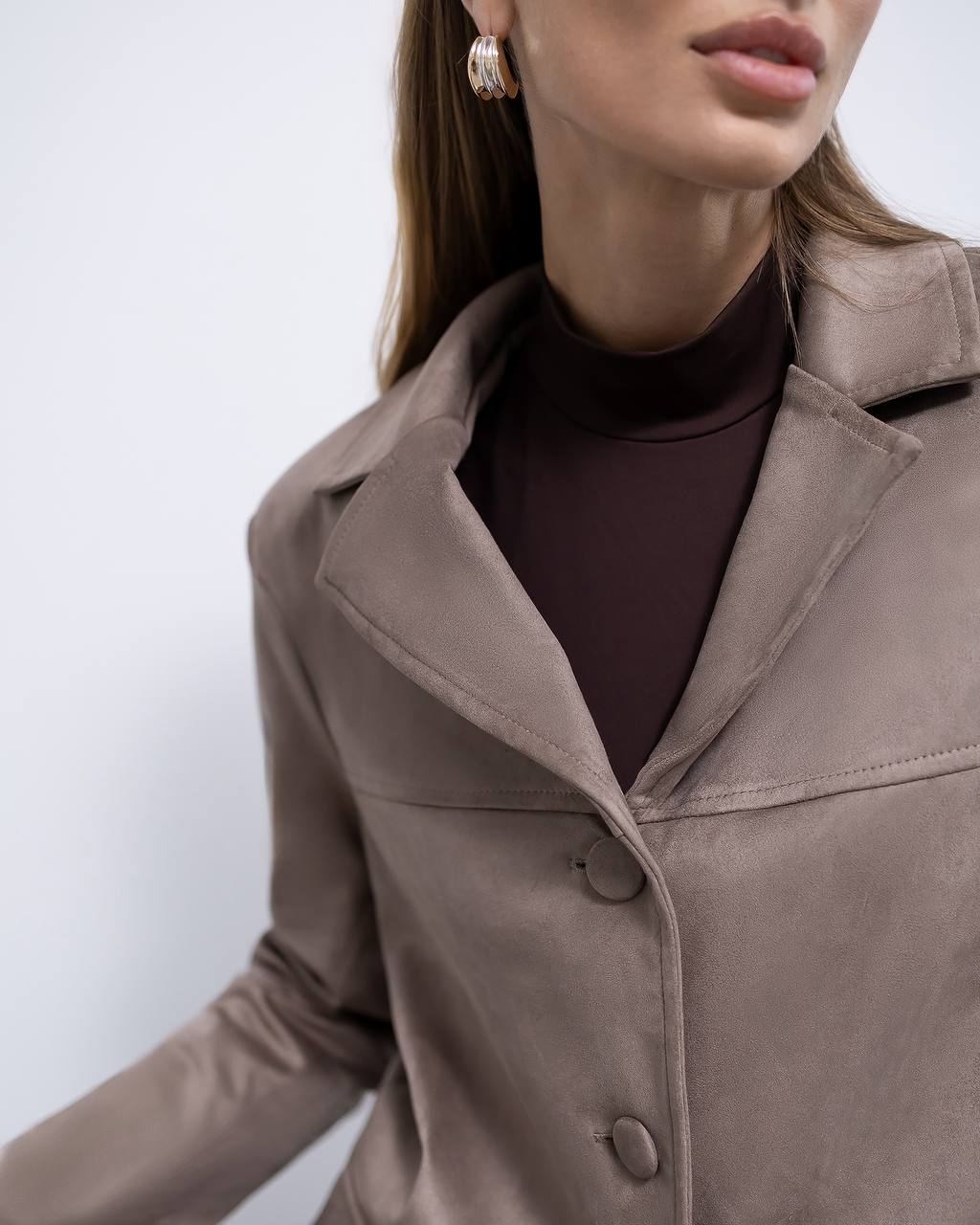 Close-up of a person wearing a brown coat with a plain background