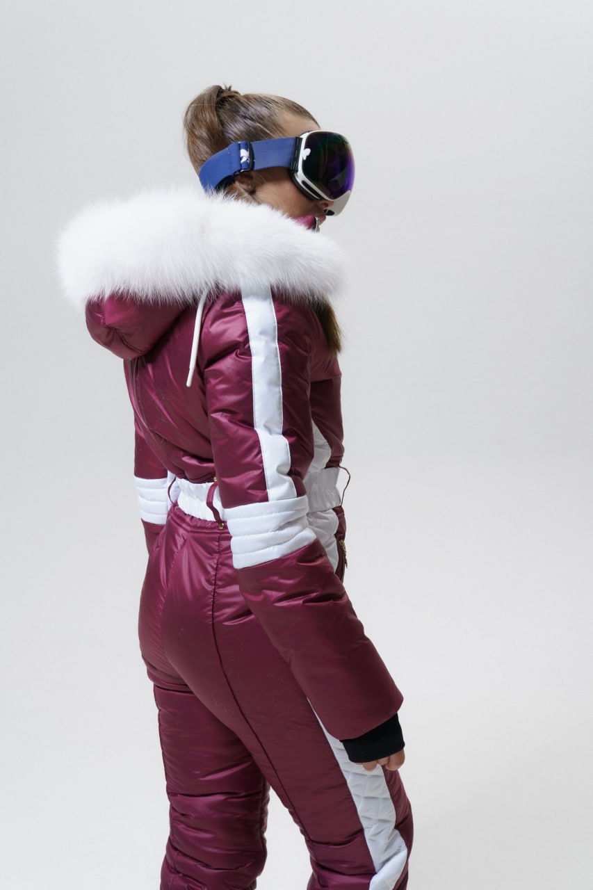 Person wearing a maroon and white ski suit with goggles on a plain background
