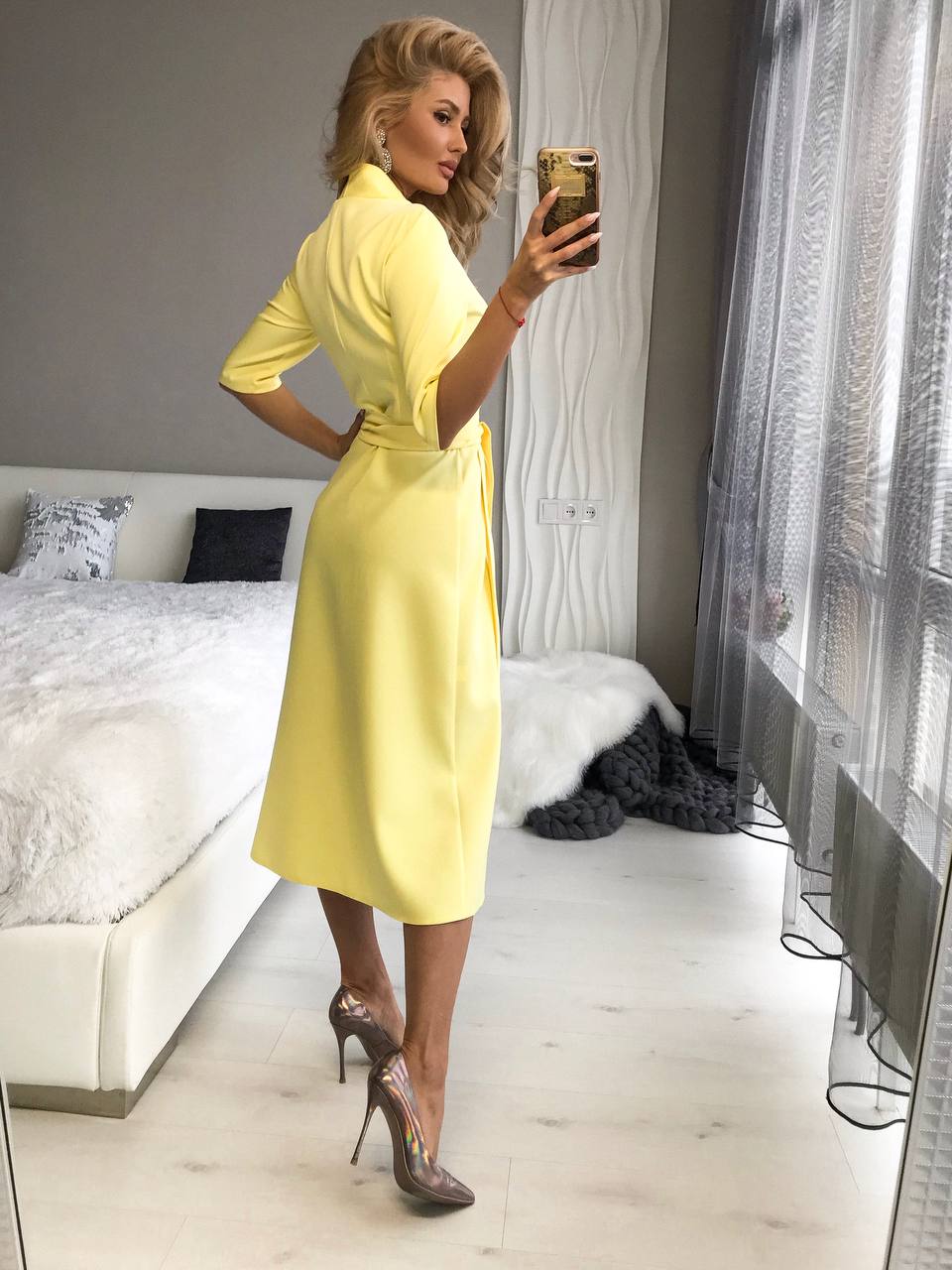 Woman in a yellow dress taking a mirror selfie in a bedroom.