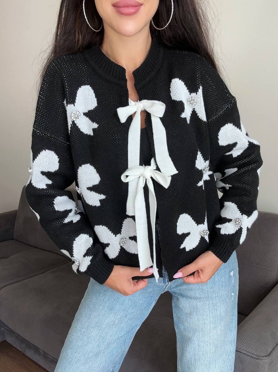 Person wearing a black sweater with white bow patterns and light blue jeans.