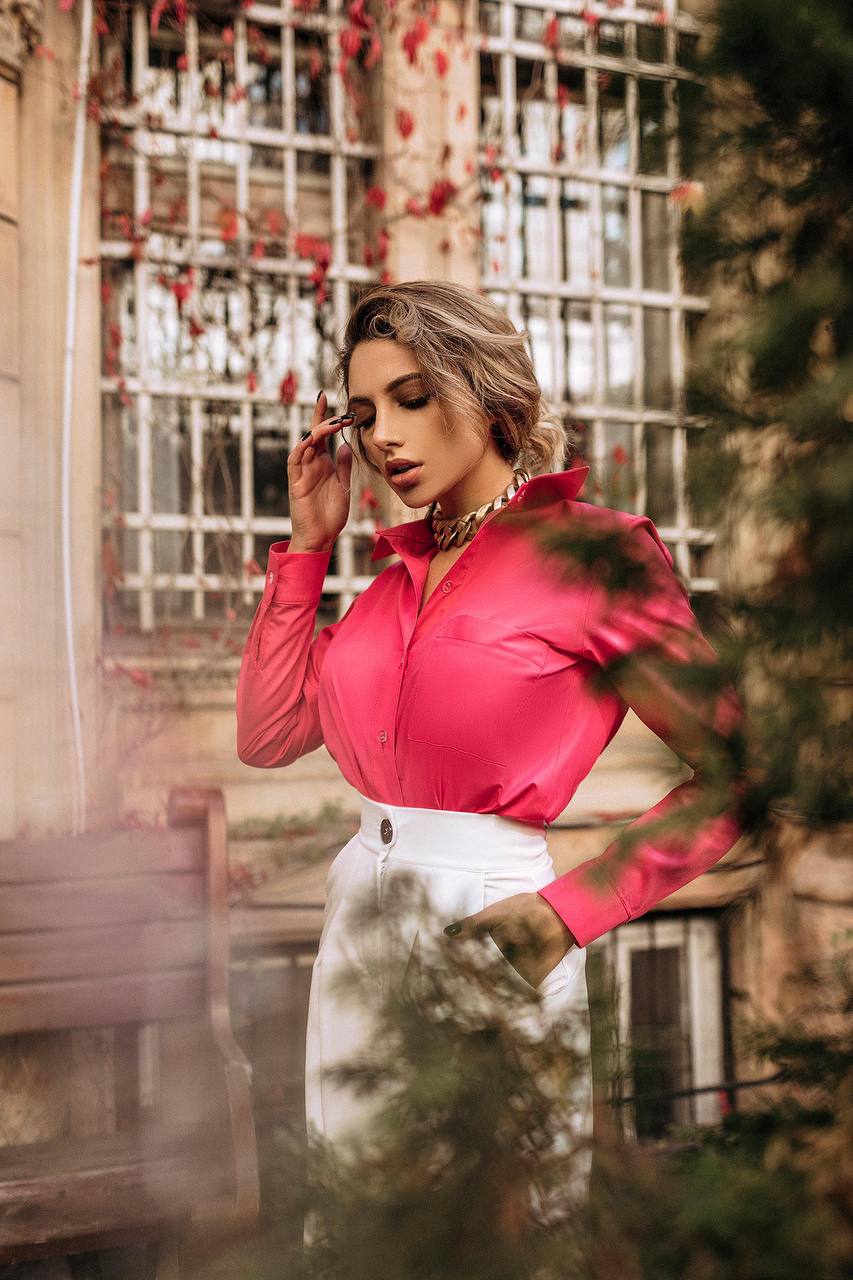 Woman wearing a bright pink blouse and white skirt outdoors with a blurred background