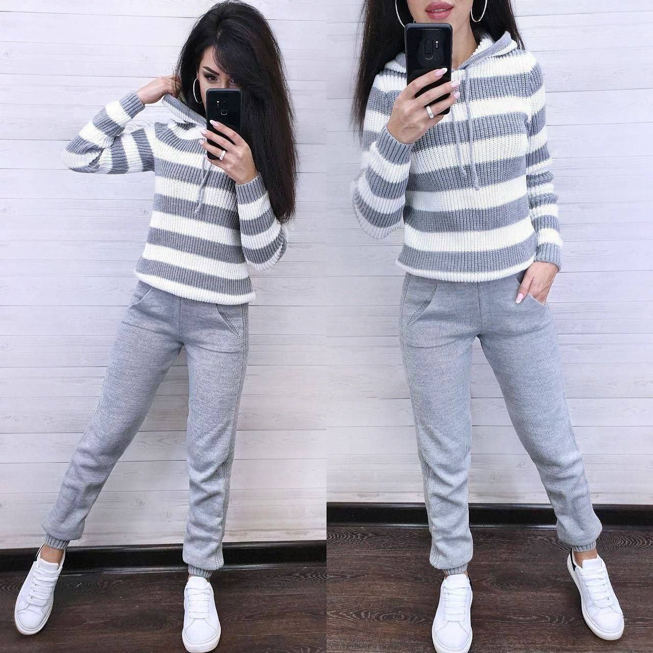 Two women wearing matching gray and white striped hoodies and gray jogger pants, standing against a white wall.