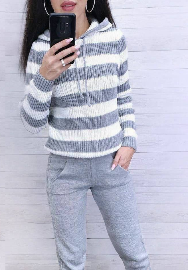 Person wearing a gray and white striped sweater and gray pants against a light wooden background.
