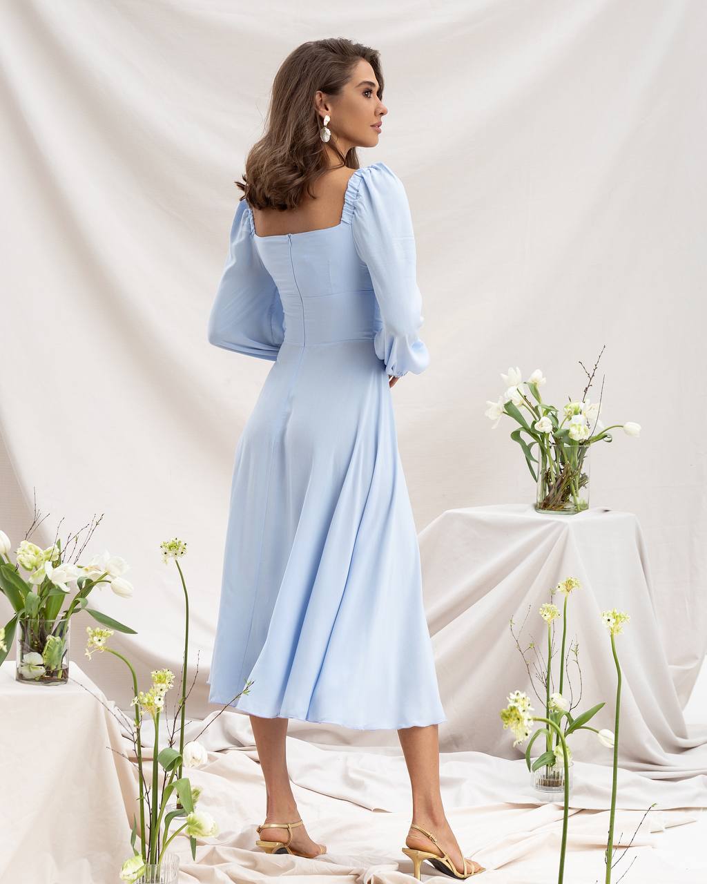 Woman in a light blue dress standing in a decorated room with flowers.
