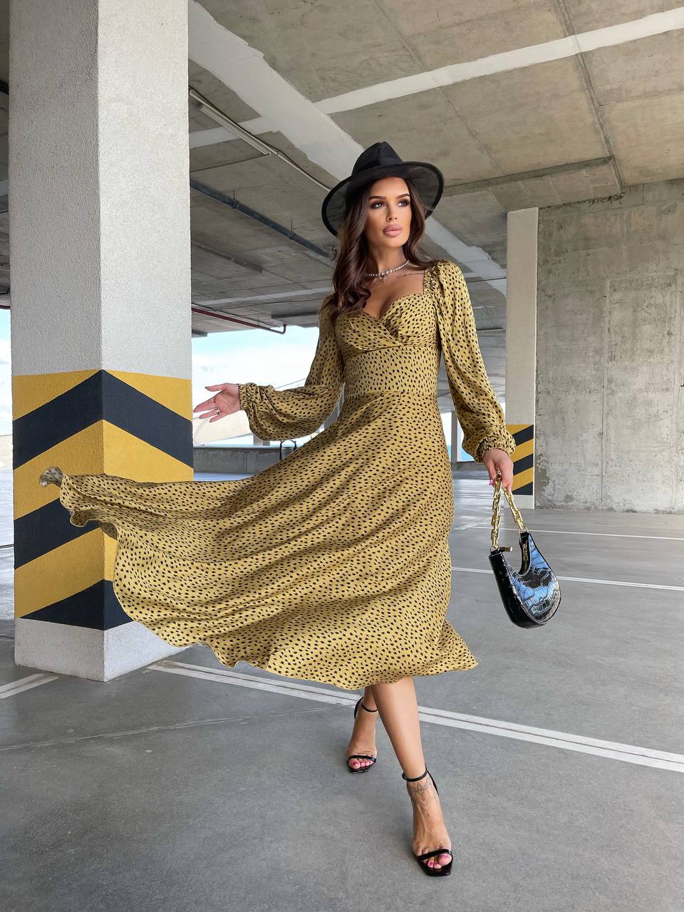 Woman in a yellow dress and black hat standing in an urban setting