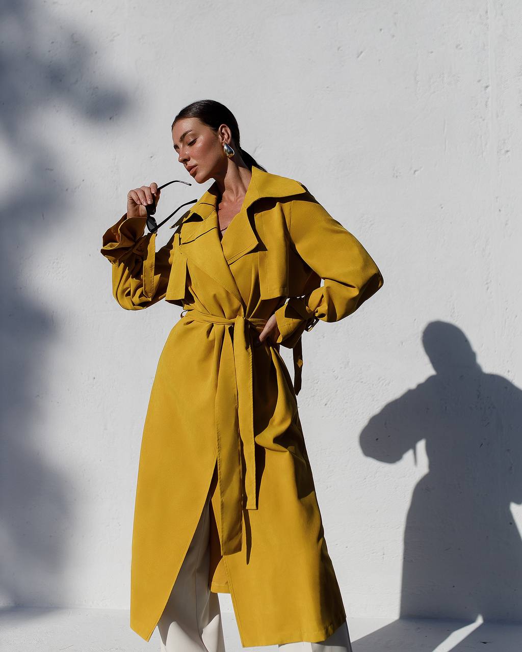 Woman wearing a yellow trench coat against a white wall