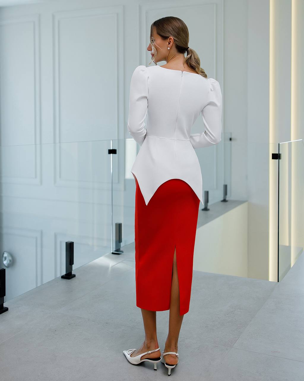 Woman wearing a white blouse and red skirt in a minimalistic room.