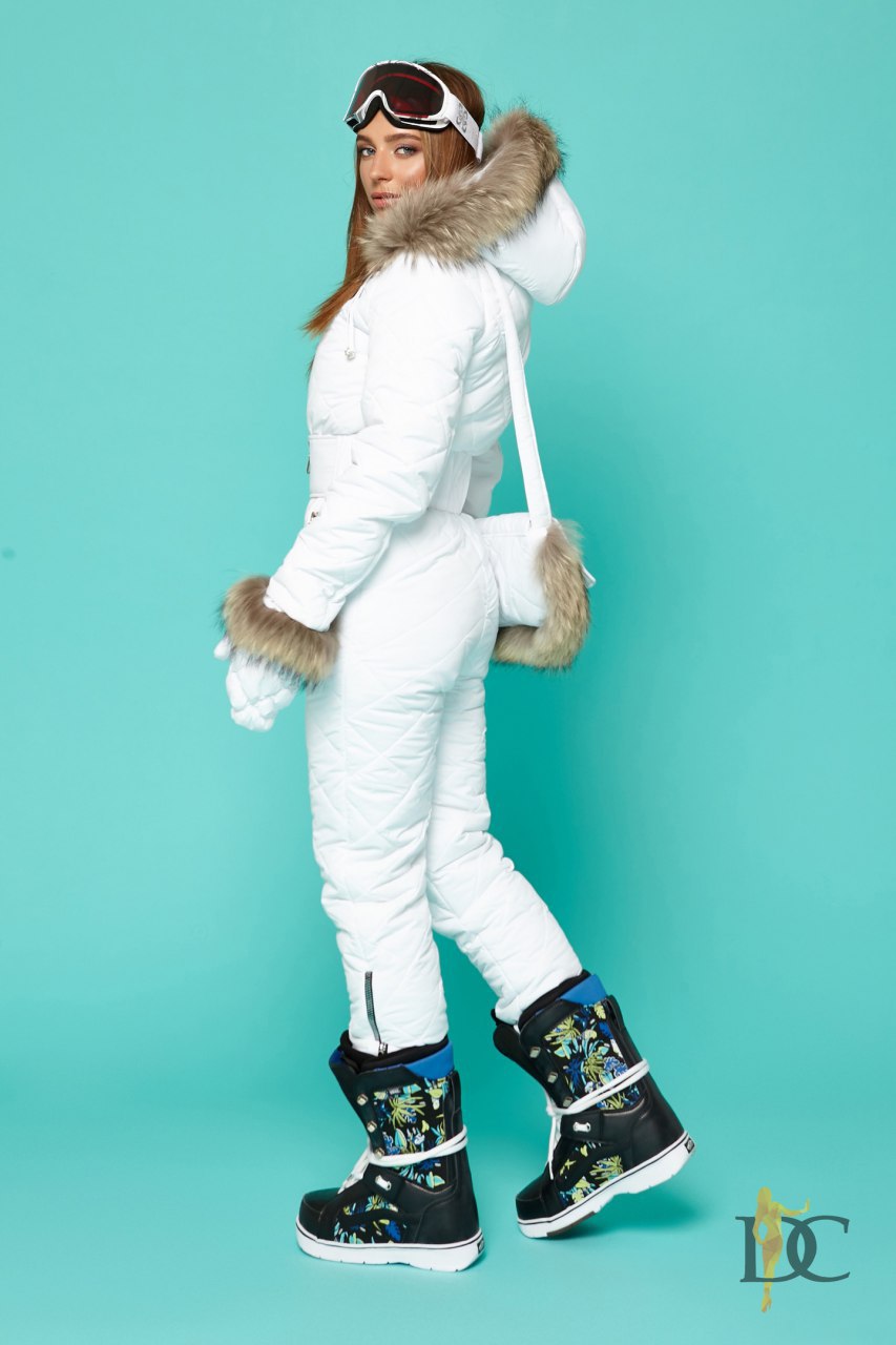 Person wearing a white winter outfit with fur-lined hood against a teal background
