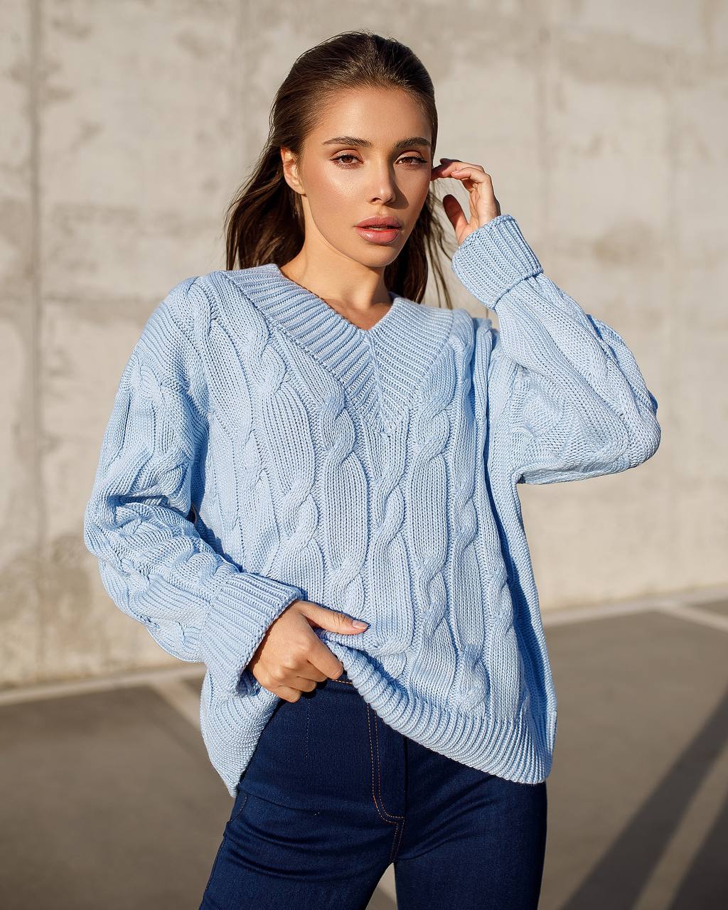 Woman wearing a light blue cable knit sweater against a neutral background