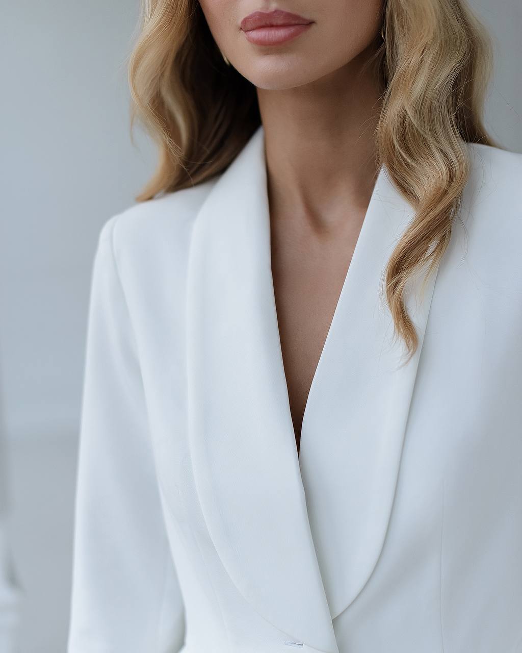 Person wearing a white blazer against a neutral background