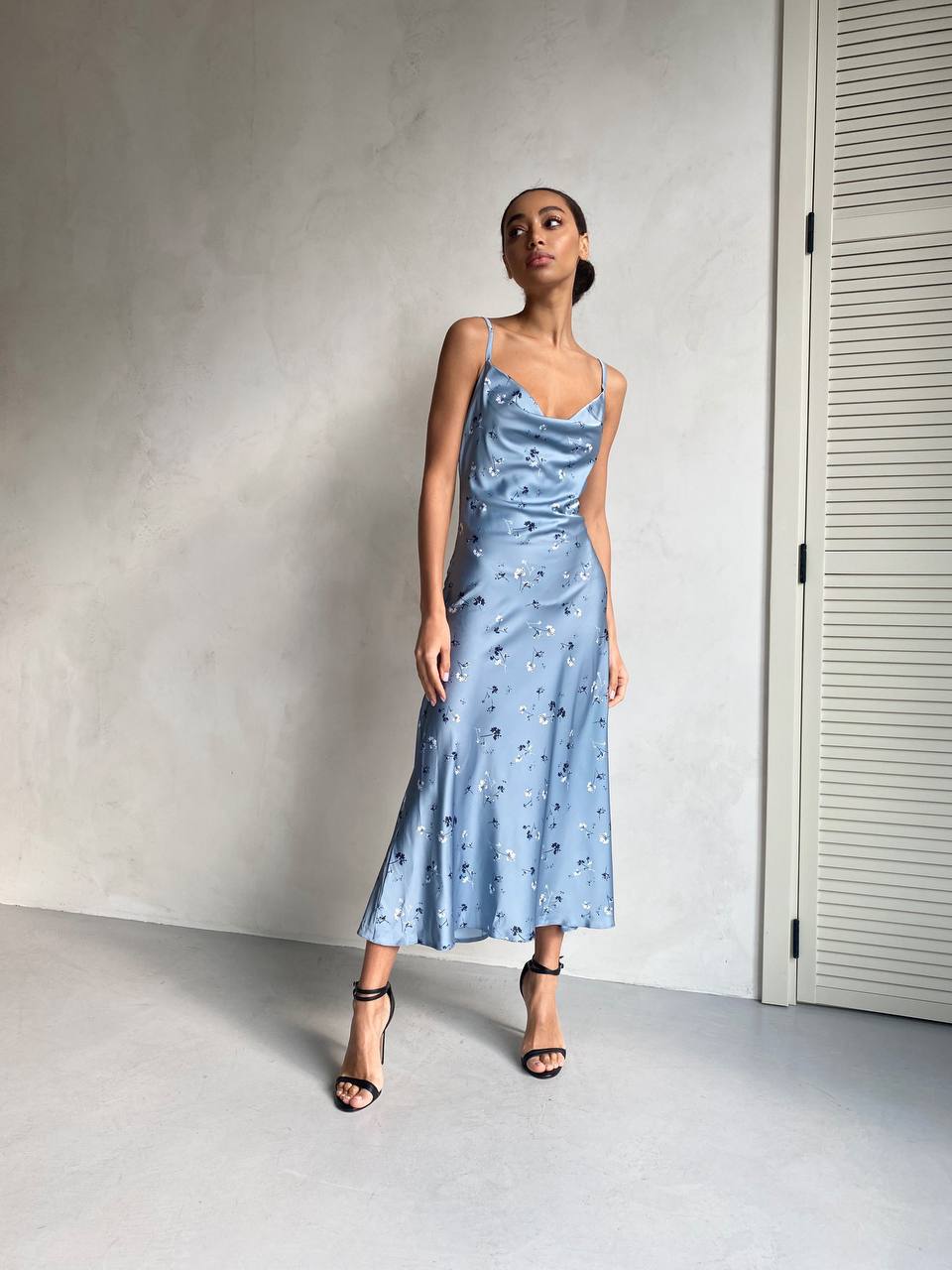 Woman wearing a light blue satin dress against a plain wall.