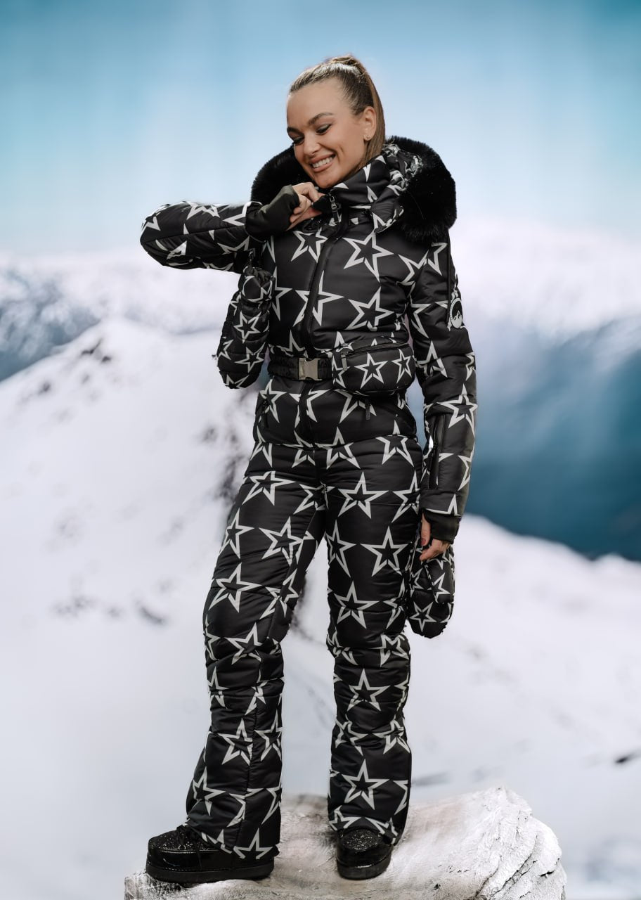 Person wearing a black snowsuit with white star patterns against a snowy mountain background