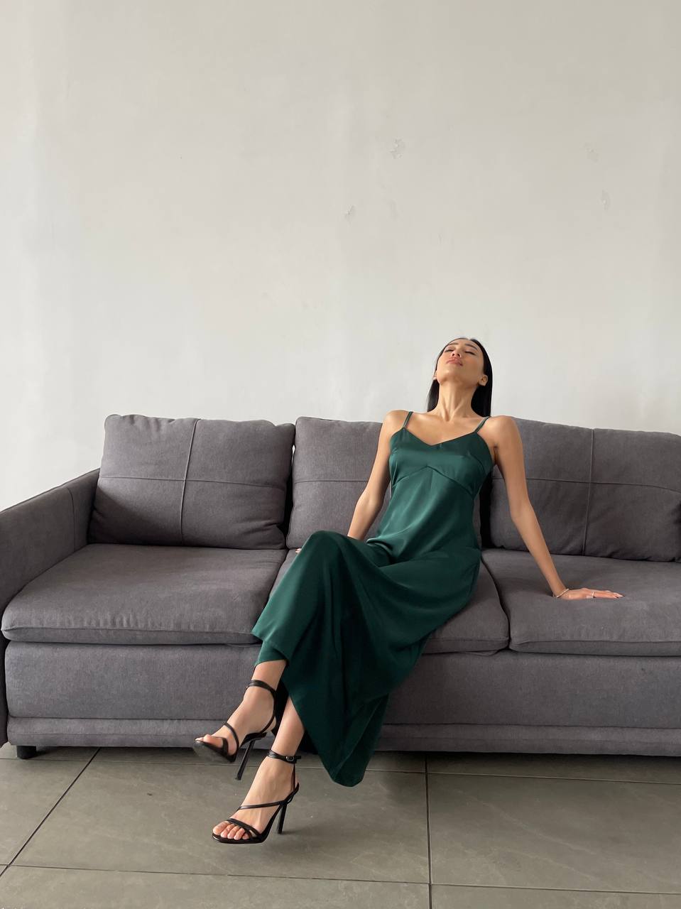 Woman in a green dress sitting on a gray sofa against a white wall.