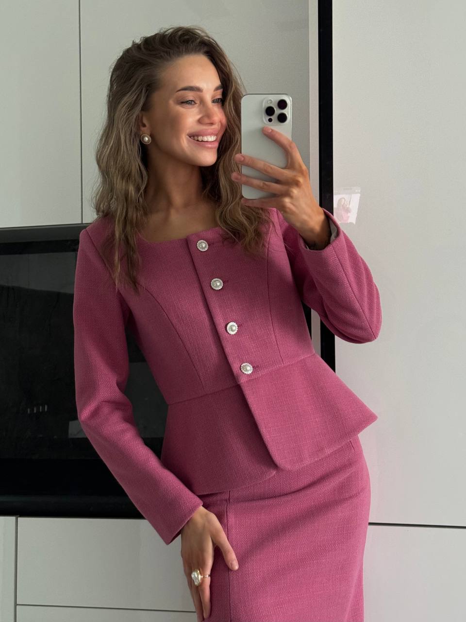 Woman taking a mirror selfie wearing a pink suit.
