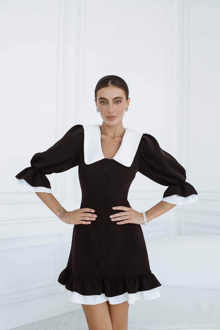 Woman wearing a black dress with white collar and cuffs against a white background