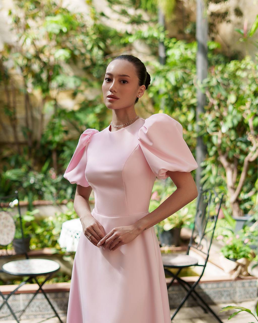 Woman in a pink dress standing outdoors with greenery in the background
