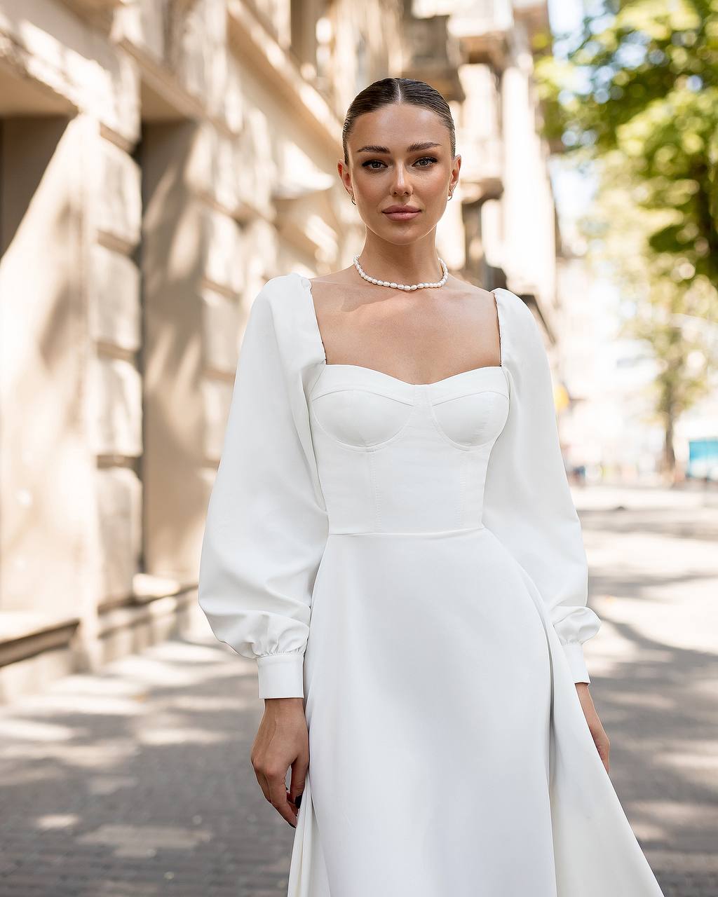 Woman wearing a white dress with long sleeves on a street.