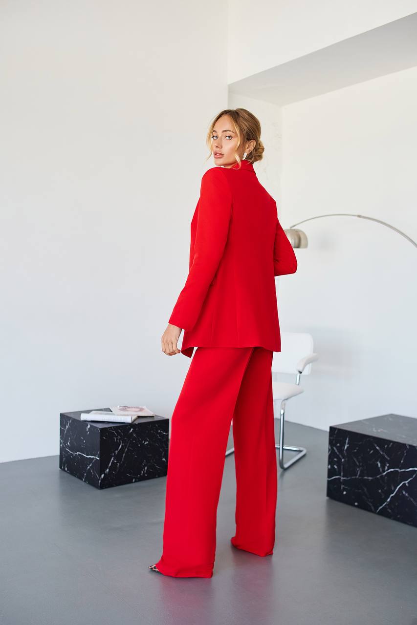 Person wearing a red suit standing in a modern room with white walls and black marble accents.