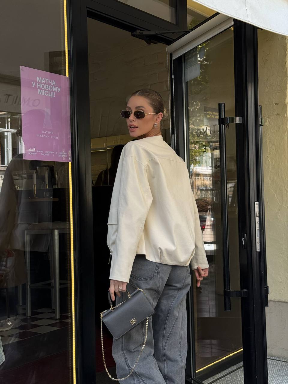Person in a white jacket and gray pants exiting a building with a purple sign on the door.