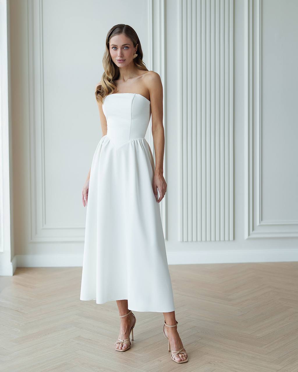 Woman wearing a white strapless dress in a minimalistic room.