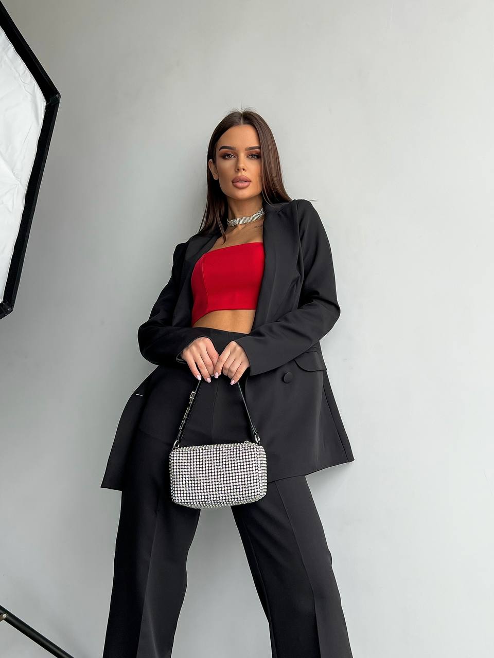 Woman in black outfit with red top holding a handbag against a white background