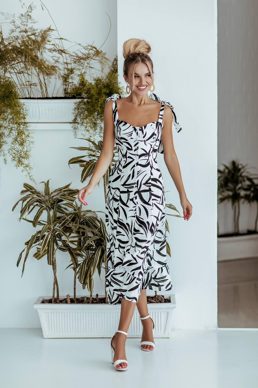 Woman in a black and white patterned dress standing in front of plants.