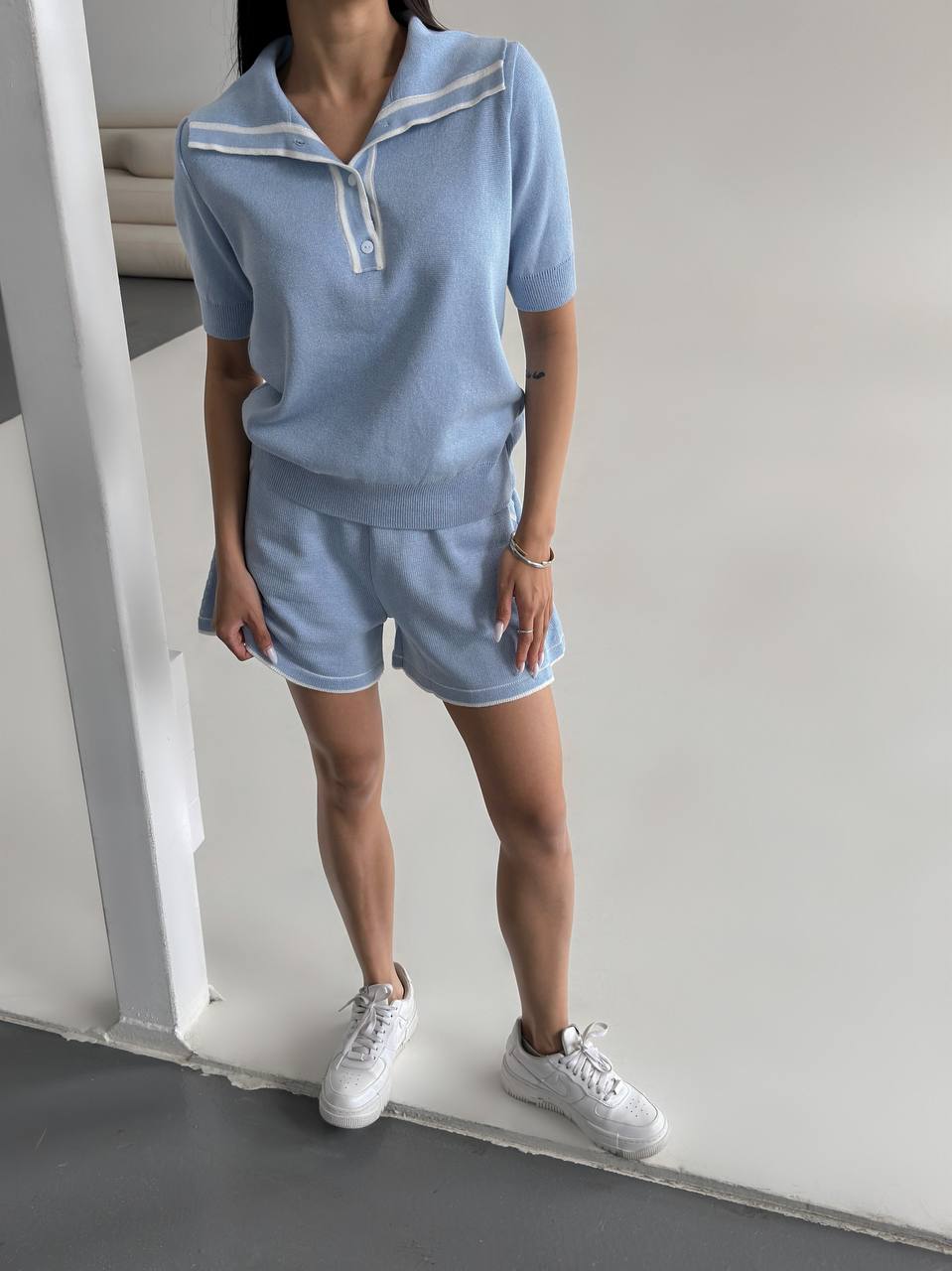 Person wearing a light blue outfit with white accents in a minimal indoor setting