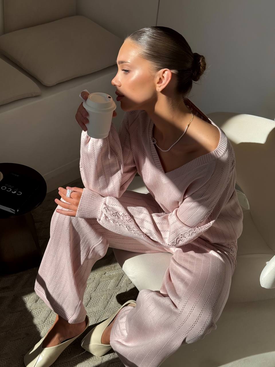 Woman in pink outfit sitting on a couch holding a coffee cup.