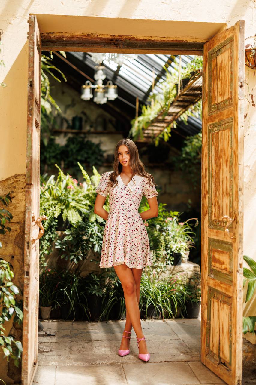 Woman in a floral dress standing in an open doorway with a garden view.
