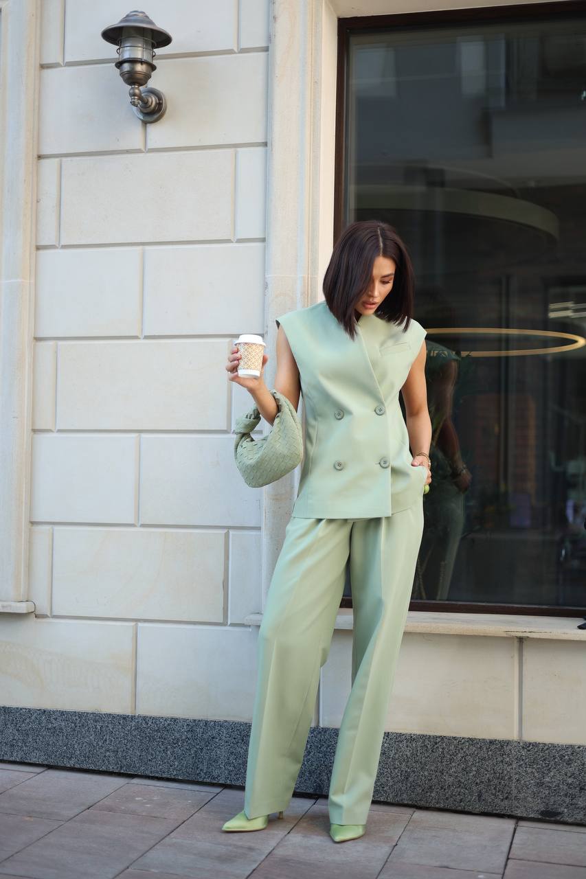 Woman in a light green outfit holding a coffee cup, standing on a sidewalk.