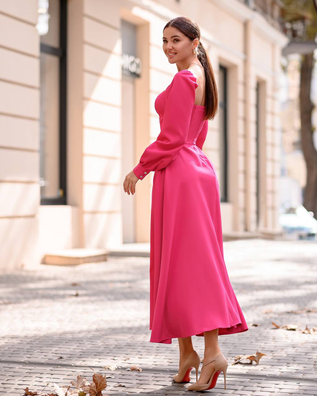 Woman in a pink dress standing on a street with buildings in the background