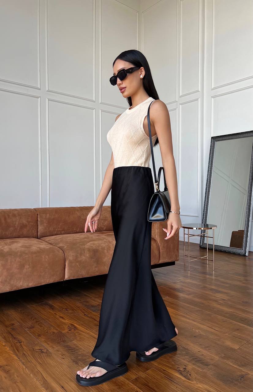 Woman in a stylish outfit with a cream top and black pants standing in a modern room.