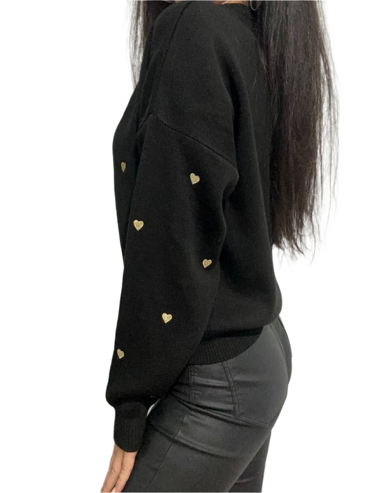 Black sweater with gold heart patterns worn by a person on a white background