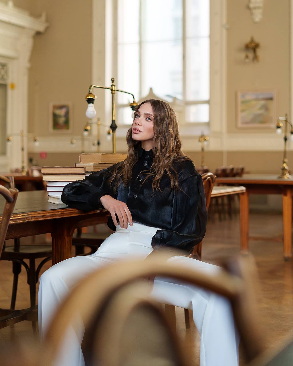 Woman sitting in a library or study room with books and wooden furniture.