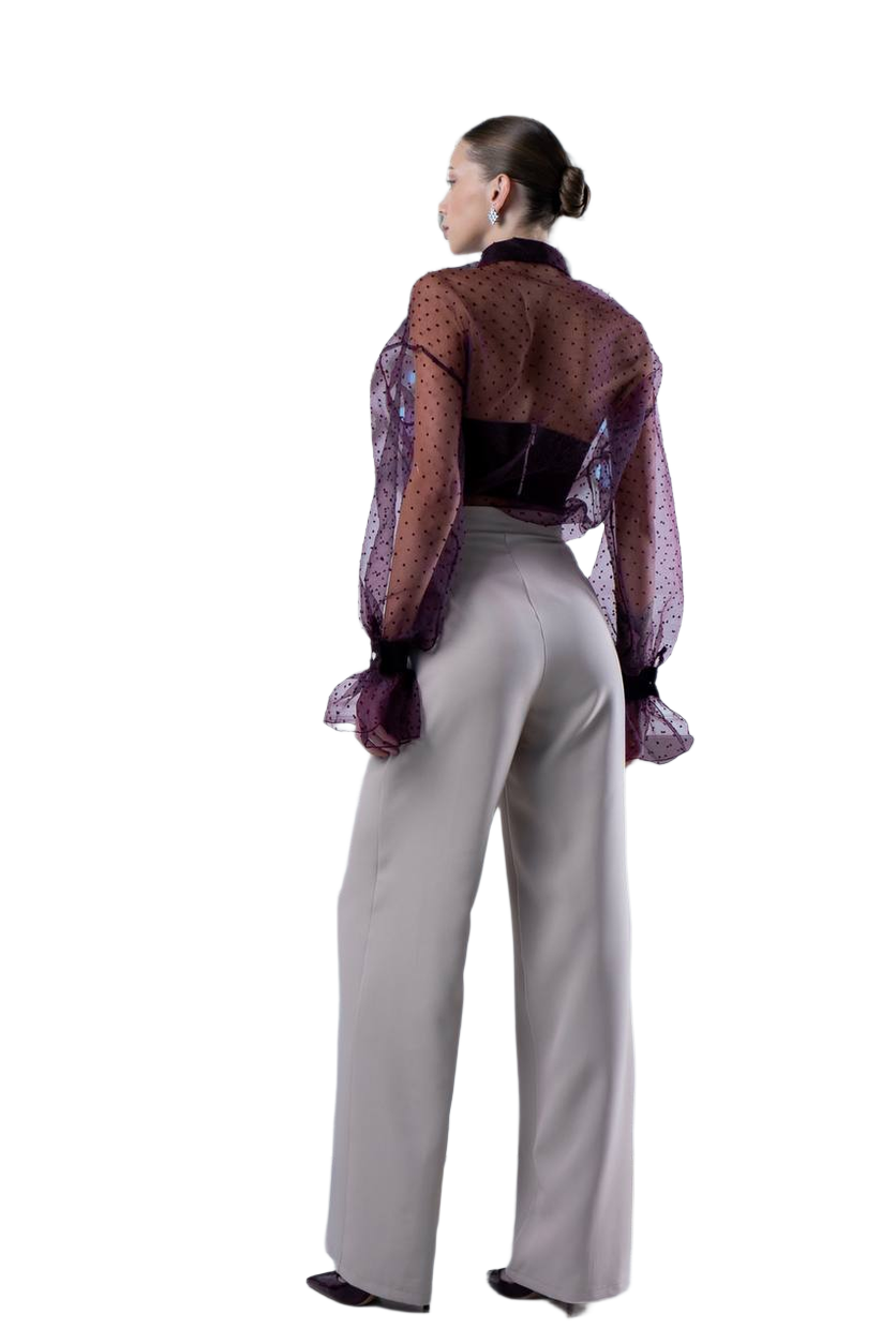 Person wearing a patterned blouse and light gray pants on a white background