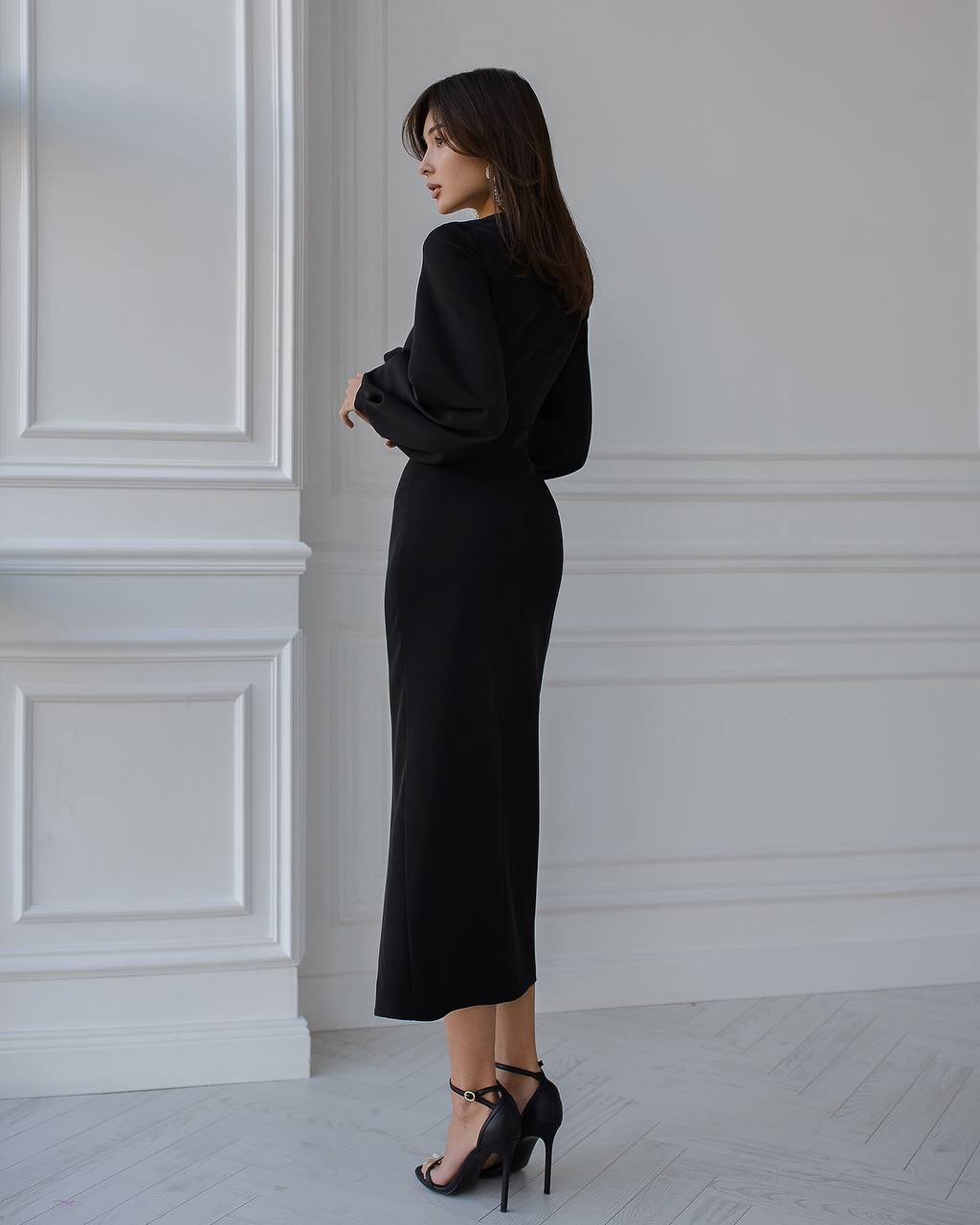 Woman wearing a black dress standing against a white wall.