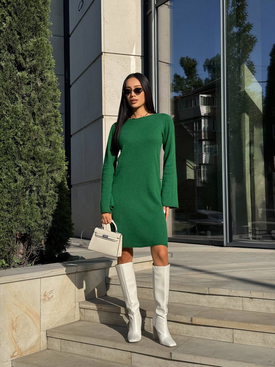 Woman in a green dress and white knee-high boots standing on steps outdoors.