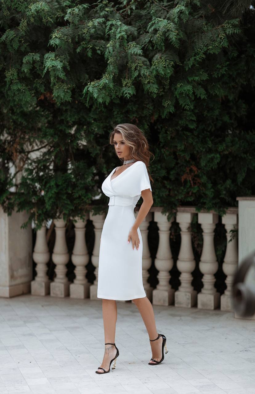 Woman in a white dress standing outdoors with greenery in the background